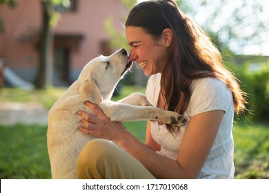Authentic shot of an young happy woman is caressing her pedigree puppy of Labrador Retriever dog while having fun together outside. Concept: love for animals, friendship, authenticity, happiness,pets