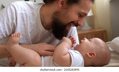 Authentic Young Bearded Man Holding Newborn Baby. Dad And Child Son On Bed. Close-up Portrait Of Smiling Family With Infant On Hands. Happy Marriage Couple On Background. Childhood, Parenthood Concept