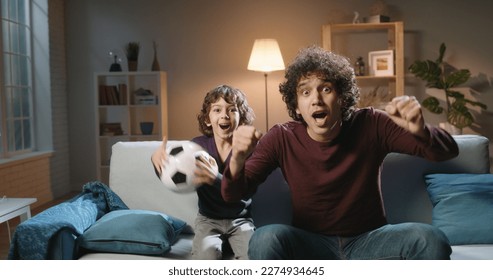 Authentic young cute asian brothers with curly hair watching soccer together, father and son reacting to victories or defeats of their team, expressing emotions - family time concept  - Powered by Shutterstock