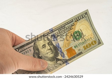 Authentication of banknote 100 dollars for clearance. Watermarks on a 100-dollar bill. Banknote in hand on a white background with a watermark. Franklin watermark on 100 bill