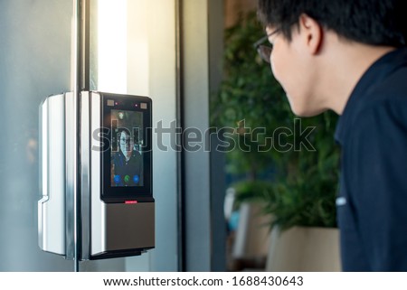 Authentication by facial recognition concept. Biometric admittance control device for security system. Asian man using face scanner to unlock glass door in office building.
