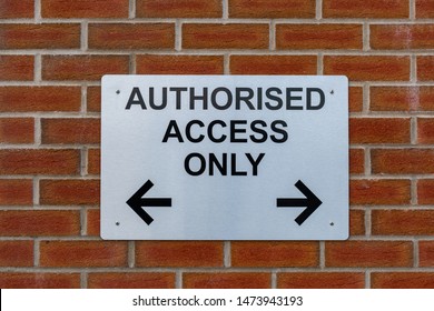 Authorised access only sign with directional arrows pointing left and  right against a red brick wall.