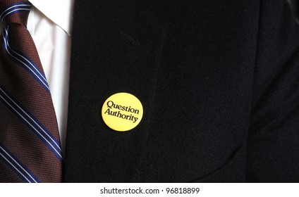 Authority Questions Authority/Close Up Of Uncopyrighted Question Authority Button Pinned To Black Camels Hair Brooks Brothers Suit Jacket With Tie & White Shirt Visible.