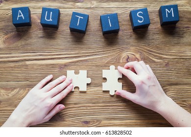 Autism awareness. Black wooden cubes with word AUTISM on a wooden background, top view, flat lay. Two hands holding puzzle pieces and connecting them. Autism Spectrum Disorder (ASD). 