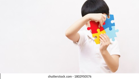 Autism awareness day April 2 - Studio Portrait of a little cute asian child cover his face with the colorful puzzles pieces. Autism Spectrum Disorder, ASD, Autistic Syndrome, Symptoms, Copy space - Powered by Shutterstock