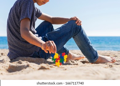 Autism Awareness Day Concept. Boy Teenager Sitting On The Beach With Colorful Puzzle Autism Awareness Heart