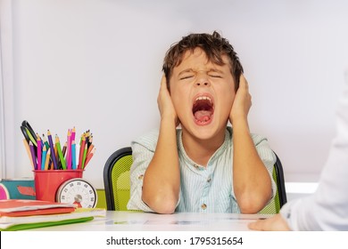 Autistic Boy Scream And Close Ears In Pain During ABA Development Therapy Sitting By The Table In Class