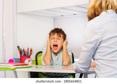 Autistic Boy Scream And Close Ears In Pain During ABA Development Therapy Sitting By The Table With Teacher