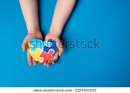 Autistic pride day concept. Child hands holding colorful puzzle heart on blue background