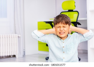 Autistic school age boy with strong negative face expression closing ears and grins teeth sitting in his room