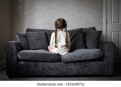 Autistic spectrum young girl sat quiet and alone with autism looking away back turned and headphones on to block out noise