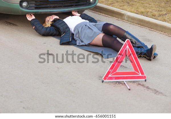 Auto assistance and insurance, troubles while
traveling concept. Woman trying to repair her broken car, checking
what is under automobile.