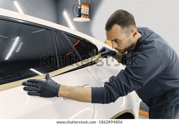 Auto body repair series. Masking car before\
repaint. Man in a black\
uniform.