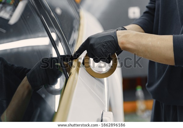 Auto body repair series. Masking car before\
repaint. Man in a black\
uniform.