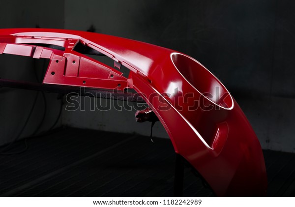 Auto body repair series: Red bumper being painted\
in paint booth