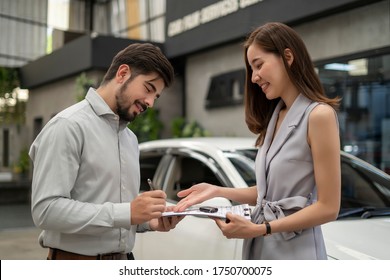 Auto Business, Car Sale, Consumerism And People Concept - Woman Sign Contract With Car Dealer In Auto Show. Car Salesman Is Making Deal With Lender. Used Cars Cheaper Than New Cars. But To Buy A Used