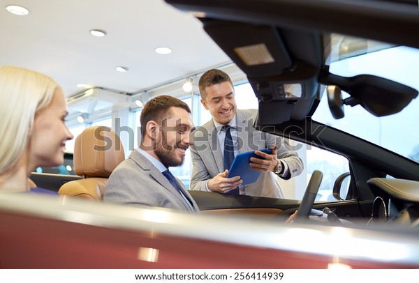 auto business, car\
sale, consumerism and people concept - happy couple with car dealer\
in auto show or salon