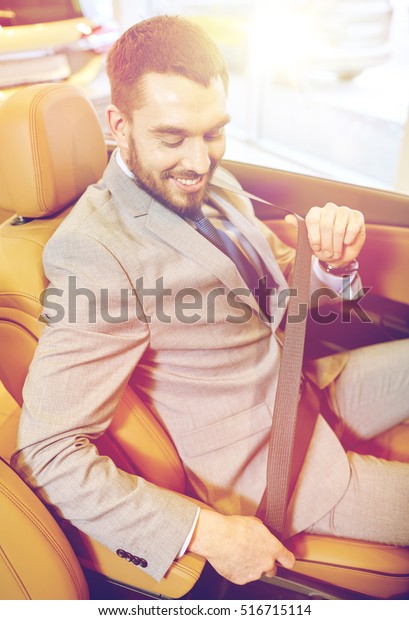 auto business, car sale, consumerism, technology\
and people concept - happy man sitting in car with smartphone at\
auto show or salon