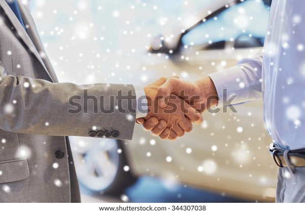 auto business, car sale, deal, gesture and people\
concept - close up of male handshake in auto show or salon over\
snow effect