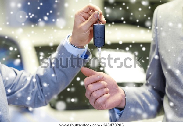 auto business, car sale, deal and people concept -
close up of male hands with car key in auto show or salon over snow
effect