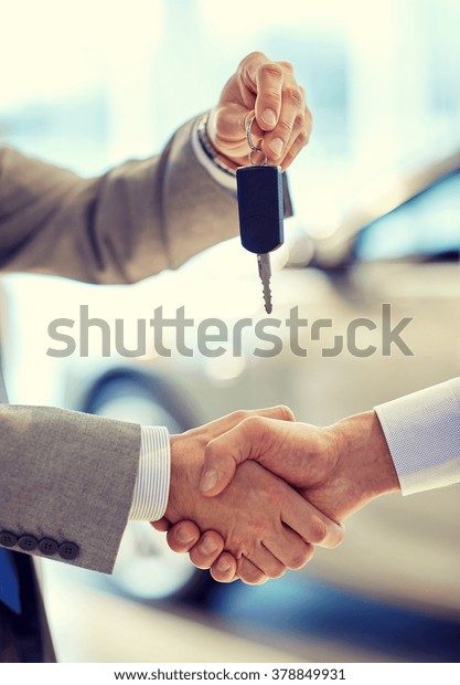auto business, car sale, deal, gesture and people\
concept - close up of dealer giving key to new owner and shaking\
hands in auto show or\
salon