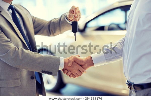 auto business, car sale, deal, gesture and people\
concept - close up of dealer giving key to new owner and shaking\
hands in auto show or\
salon