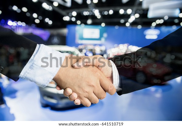Auto business, car\
sale, deal, gesture and people concept - Close up of male handshake\
in auto show or salon