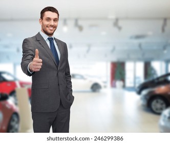 Auto Business, Car Sale, Gesture And People Concept - Smiling Businessman Showing Thumbs Up Over Auto Show Background