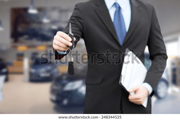 auto business, car sale, gesture and\
people concept - close up of businessman or salesman with documents\
giving car key over auto show\
background
