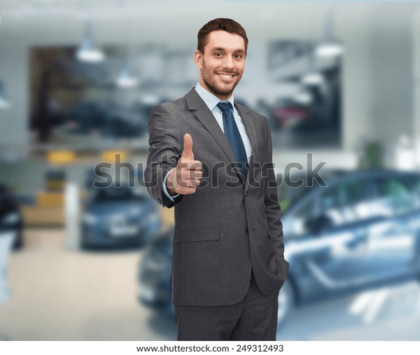 auto business, car sale, gesture and people\
concept - smiling businessman showing thumbs up over auto show\
background