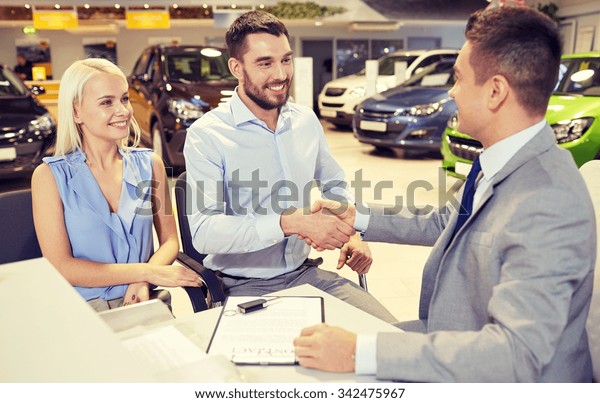 auto business, car\
sale, and people concept - happy couple with dealer shaking hands\
in auto show or salon