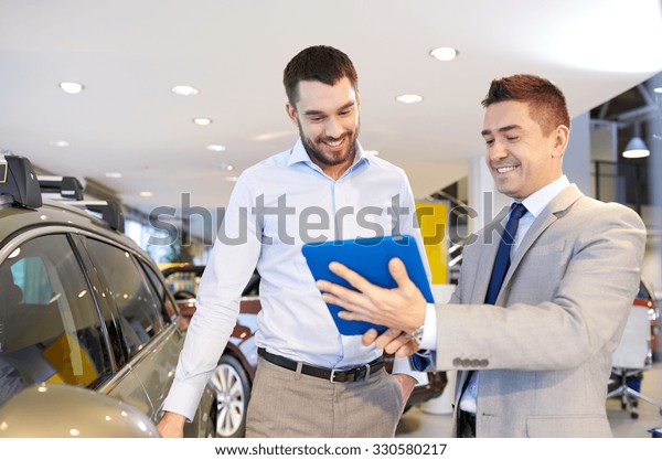 auto business, car sale, technology and people\
concept - happy man and car dealer with tablet pc computer in auto\
show or salon