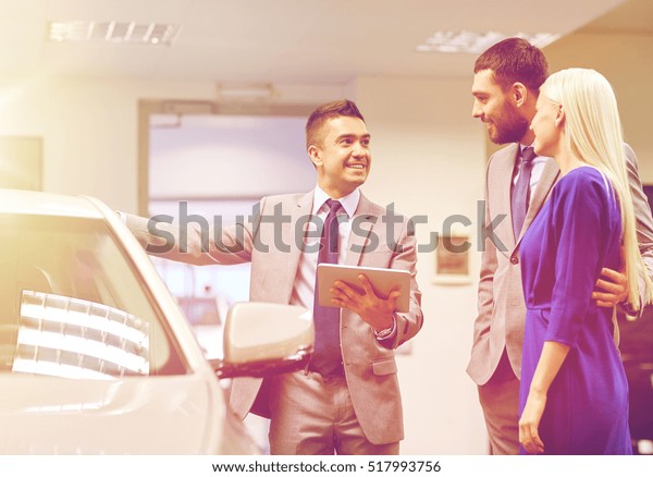 auto business, car\
sale, technology and people concept - happy couple with car dealer\
in auto show or salon