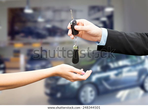 auto business, car sale,\
transportation, people and ownership concept - close up of car\
salesman giving key to new owner or customer over auto show\
background