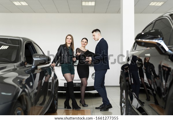 Auto business,\
car sales - a couple of friends of girls with a car dealer choose a\
car in a car dealership