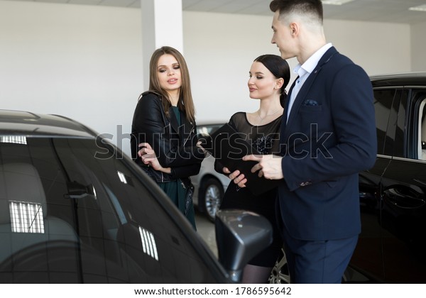 Auto business,
car sales - a couple of friends of girls with a car dealer choose a
car in a car dealership
