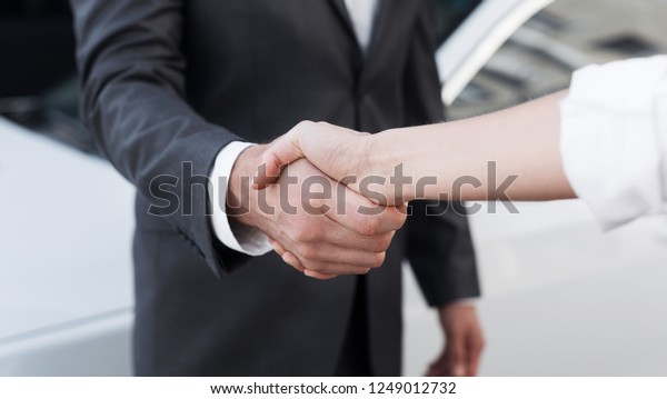 Auto business. Female salesman\
shaking hands with customer in successful dealership,\
closeup