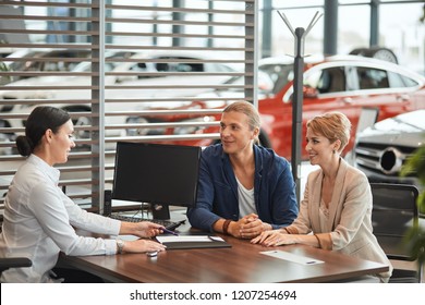 Auto Business, Sale And People Concept - Happy Caucasian Couple Buying Car And Sales Rep Female Suggest To Sign A Form Of A Vehicle Sales Agreement At Car Dealership