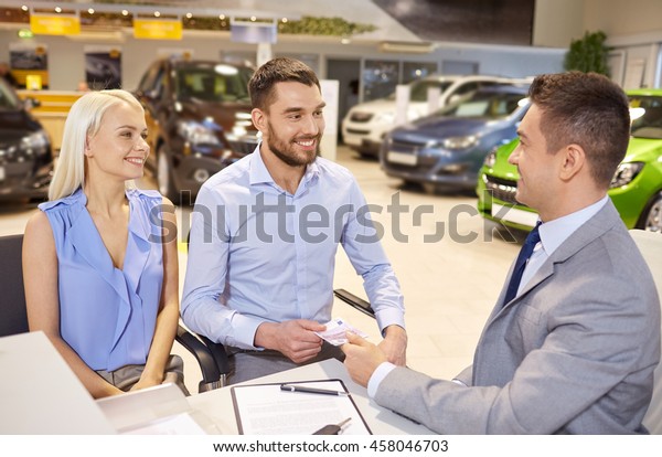 auto business, sale and people\
concept - happy couple with dealer buying car in auto show or\
salon