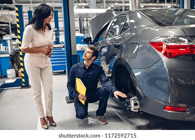 Auto Car Repair Service Center. A Female Customer And Mechanic Checking Car Breaks