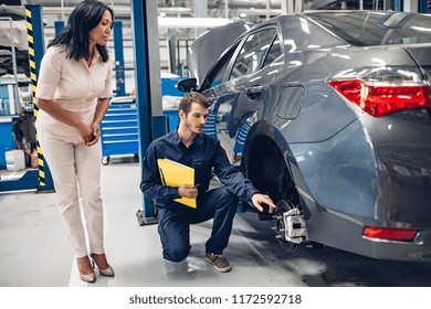 Auto Car Repair Service Center. A Female Customer And Mechanic Checking Car Breaks