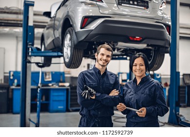 Auto Car Repair Service Center. Two Happy Mechanics - Man And Woman Standing By The Car