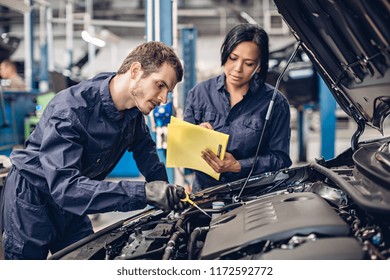 Auto Car Repair Service Center. Two Mechanics - Man And Woman Examining Car Engine