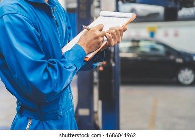 Auto Check Up And Car Service Shop Concept. Mechanic Writing Job Checklist To Clipboard To Estimate Repair Quotation To Client At Workshop Garage.