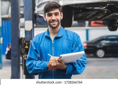 Auto Check Up And Car Service Shop Concept. Mechanic Writing Job Checklist To Clipboard To Estimate Repair Quotation To Client At Workshop Garage.