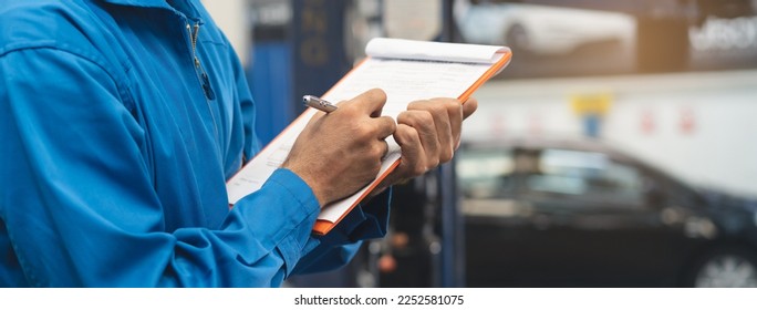 Auto check up and car service shop concept. Mechanic writing job checklist to clipboard to estimate repair quotation to client at workshop garage. - Powered by Shutterstock