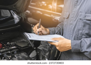 Auto check up and car service shop concept. Mechanic writing job checklist to clipboard to estimate repair quotation to client at workshop garage.
