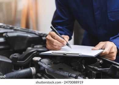 Auto check up and car service shop concept. Mechanic writing job checklist to clipboard to estimate repair quotation to client at workshop garage. - Powered by Shutterstock