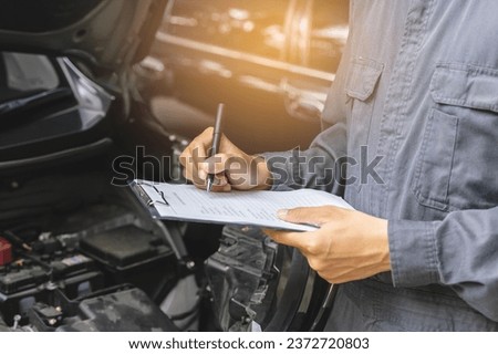 Auto check up and car service shop concept. Mechanic writing job checklist to clipboard to estimate repair quotation to client at workshop garage.