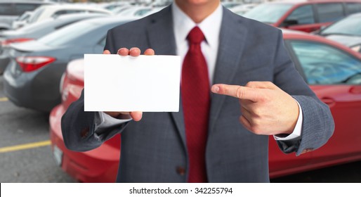 Auto dealer with a business card over vehicles background.